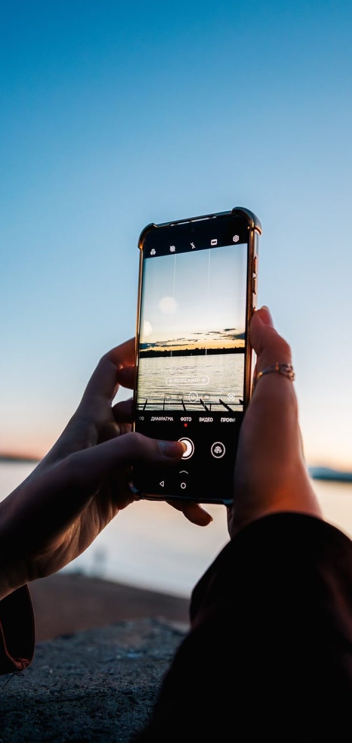 草料 App 在手机屏幕上打开二维码编辑页面的实拍效果，界面顶部是草料标志，中部是正在生成的活码预览图，背景是暖色调工作台环境，光线柔和明亮